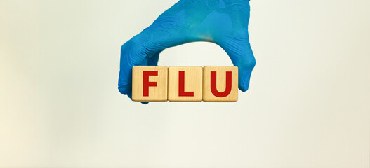 Medical and COVID-19 Pandemic Coronavirus concept. Hand in blue glove holds wooden cubes with the inscription 'FLU'. Beautiful white background. Copy space.