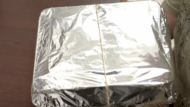Woman's hands tying bow of twine on box wrapped in foil. HD