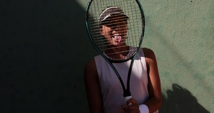 Female tennis player smiling through racket with tongue out