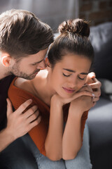 young man embracing depressed girlfriend while calming hear at home