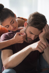 responsive woman touching face of depressed boyfriend sitting on sofa with bowed head