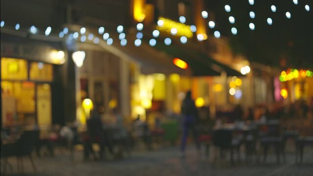 Slow motion shot of illuminated street with cafes and summer terraces. People walk along the pedestrian street of the old city and choose a place for dinner. Cozy restaurants for a romantic evening