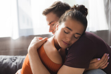 young, tender couple hugging with closed eyes while sitting at home