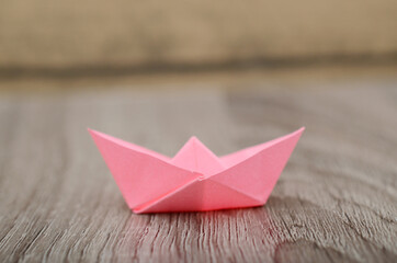 Origami pink paper boat isolated on woden background