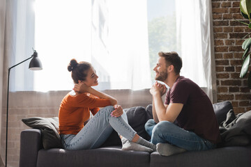 side view of young couple sitting on sofa and talking while looking at each other - Powered by Adobe