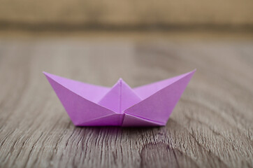 Origami violet paper boat isolated on woden background