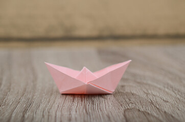 Origami pink paper boat isolated on woden background