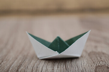 Origami green white paper boat isolated on woden background