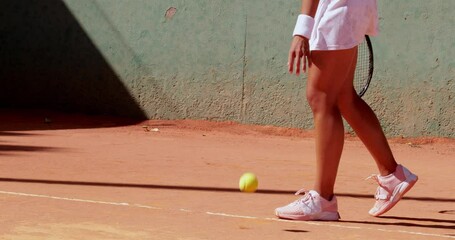 Mid-low section of woman bouncing ball on tennis court