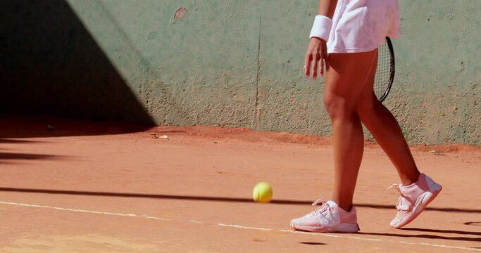 Mid-low section of woman bouncing ball on tennis court