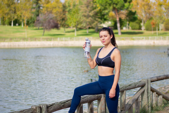 Instructor de fitness mujer delgada hermosa caucásica agua potable durante los ejercicios de entrenamiento al aire libre. mujer en ropa deportiva