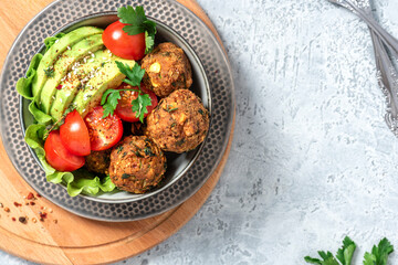 Homemade falafel with vegetables. Chickpea balls with spices, tomatoes and avocado in a bowl on a gray concrete table top view. Free space for text. Arabic cuisine, vegetarian food. Copy space.