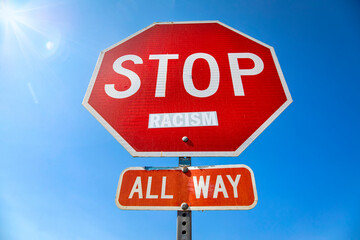 A stop sign with the word racism attached to the sign.