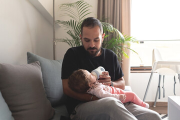 Father feeding bottle milk to baby daughter at home