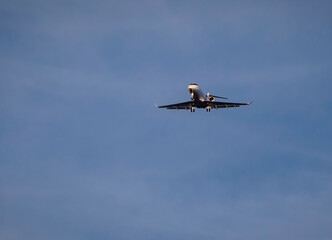 Private jet with landing gear down flying across blue sky with white cirrus clouds. Negative space is availalble.