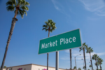A green street sign that says Marketplace with palm trees and a blue sky background