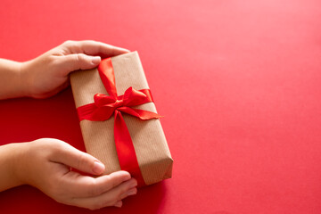 High angle of hands diagonally holding present box wrapped with red ribbon isolated over red background