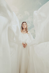 Beautiful mysterious woman in white dress. Beautiful sorceress princess against sky clouds background