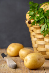Close-up of basket with yellow potatoes, parsley, potatoes and knife, on rustic table, with black background, in vertical, with copy space