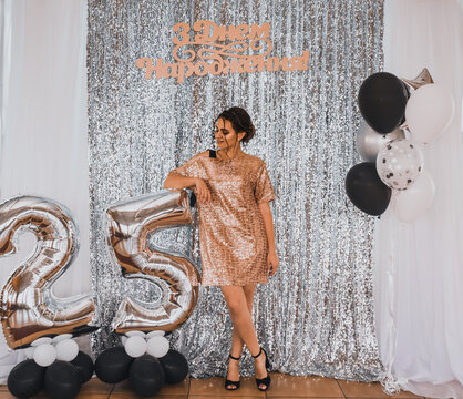 inscription: happy birthday. 25th birthday woman with a balloon. Fashion summer 2021 style glamorous. Light casual hairstyle for women with perm.Shiny festive silver photo zone with balloons
