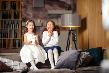 Naklejka premium Two beautiful little girls are sitting on the back of sofa.