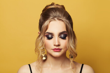 Beautiful young woman face with trendy fashionable makeup on yellow background