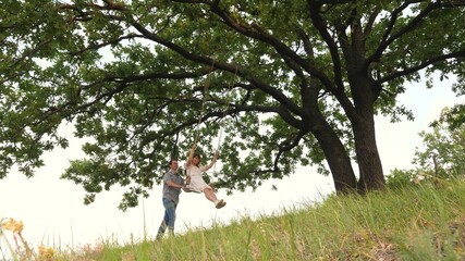 Naklejka na ściany i meble Happy girl swinging on a swing in the park on a large oak tree. Freedom of flight
