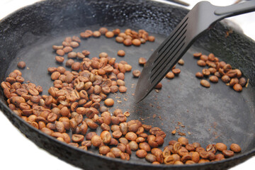 Green coffee beans roasting on the black pan