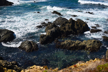 rocks in the turquoise ocean with sea foam in california