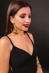 Fototapeta premium Beautiful woman in black dress is looking down with smile on black background
