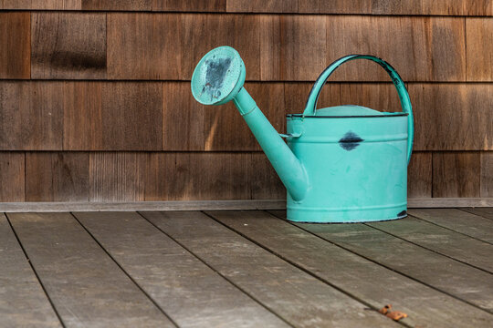 old fashioned turquoise watering can on a wooden porch