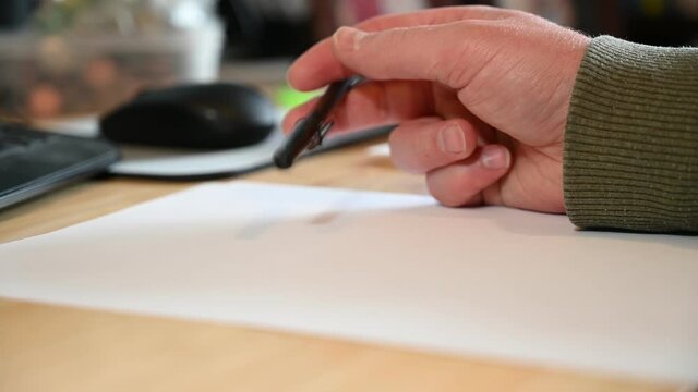 Nervously tapping a pen on a pad of paper in a home office with a defocused mouse and keyboard in the background