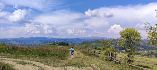 Fototapeta na wymiar The girl with backpack walks along the road in the mountains. Yasinia. Carpathians. Ukraine. Europe