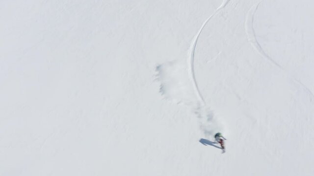 Snowboarder fast freeride riding on snowboard on snowy slope at winter mountain view from drone. Aerial view people snowboarding on snowy resort. Sport people activity on winter vacation