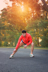 Runner stretching on road with vegetation in the background at sunset. Sportswear. Healthy life.