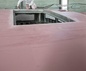 Painters putying filler and working on a super sailing yacht. Ship building industry. Shipyard.