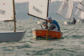 Sailor in a sailboat on a competition in Optimist class on open waters on the sea during sunny weather.