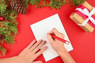 Female hands holding going to write letter to Santa. Christmas decorations on red desk. 