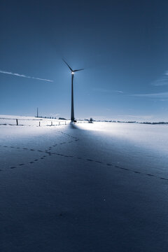Wind Turbine in winter on a field with sunflare and shadows of the blades