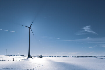 Wind Turbine in winter on a field with sunflare and shadows of the blades