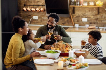 Happy black family toasting during Thanksgiving lunch in dining room.