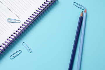 Blue wooden pencils, blue paper clips and a notebook over a bright blue background.