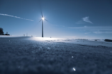 Wind Turbine in winter on a field with sunflare and shadows of the blades