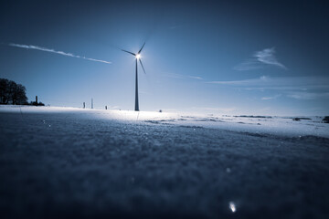 Wind Turbine in winter on a field with sunflare and shadows of the blades
