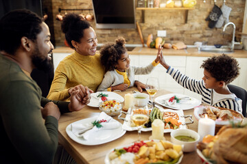 Happy African American siblings giving high-five during Thanksgiving lunch in dining room.