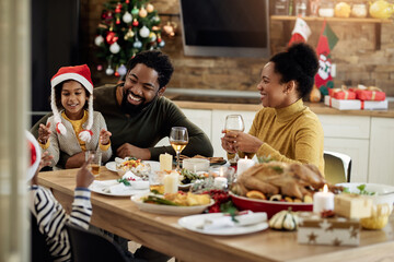 Happy African American family talking during Christmas lunch at dining table.