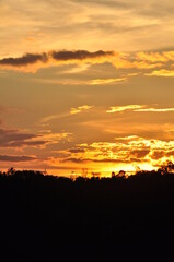 Fototapeta premium Picture of a sun setting behind a dense forest area followed by mountains. 