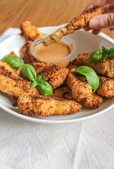 Chicken finger being dipped into the sauce. breaded and baked chicken finger eaten as an appetiser. Female hand holding chicken finger. 