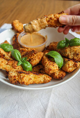 Chicken finger being dipped into the sauce. breaded and baked chicken finger eaten as an appetiser. Female hand holding chicken finger. 