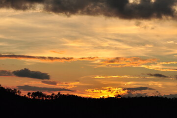 Picture of a sun setting behind a dense forest area followed by mountains.	